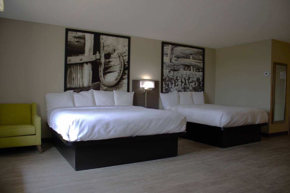 A hotel room with two beds, a bedside table, a lamp, and a yellow armchair.