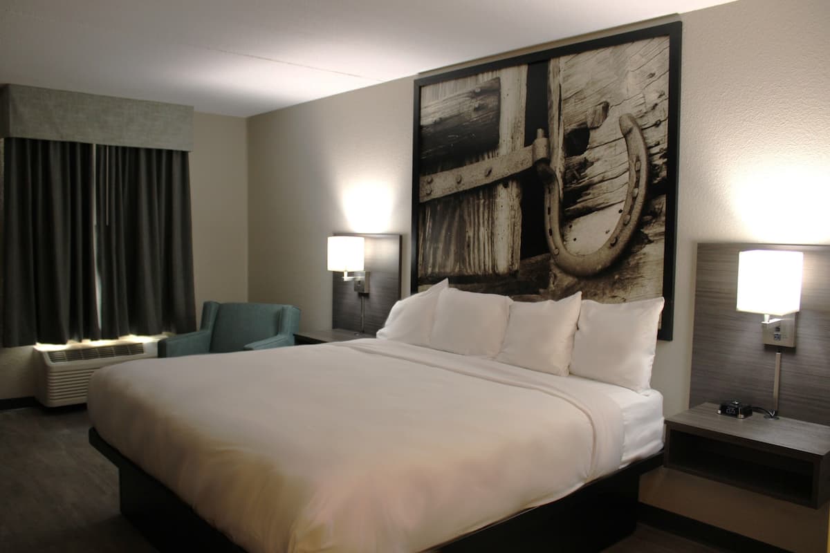 A hotel room with a large bed, two bedside lamps, a chair, and a wall-mounted air conditioner.