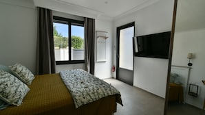 A hotel room with a bed, a TV, a window with curtains, and a door. - Chambre D'hôtes Une Nuit en Luberon (Puyvert)