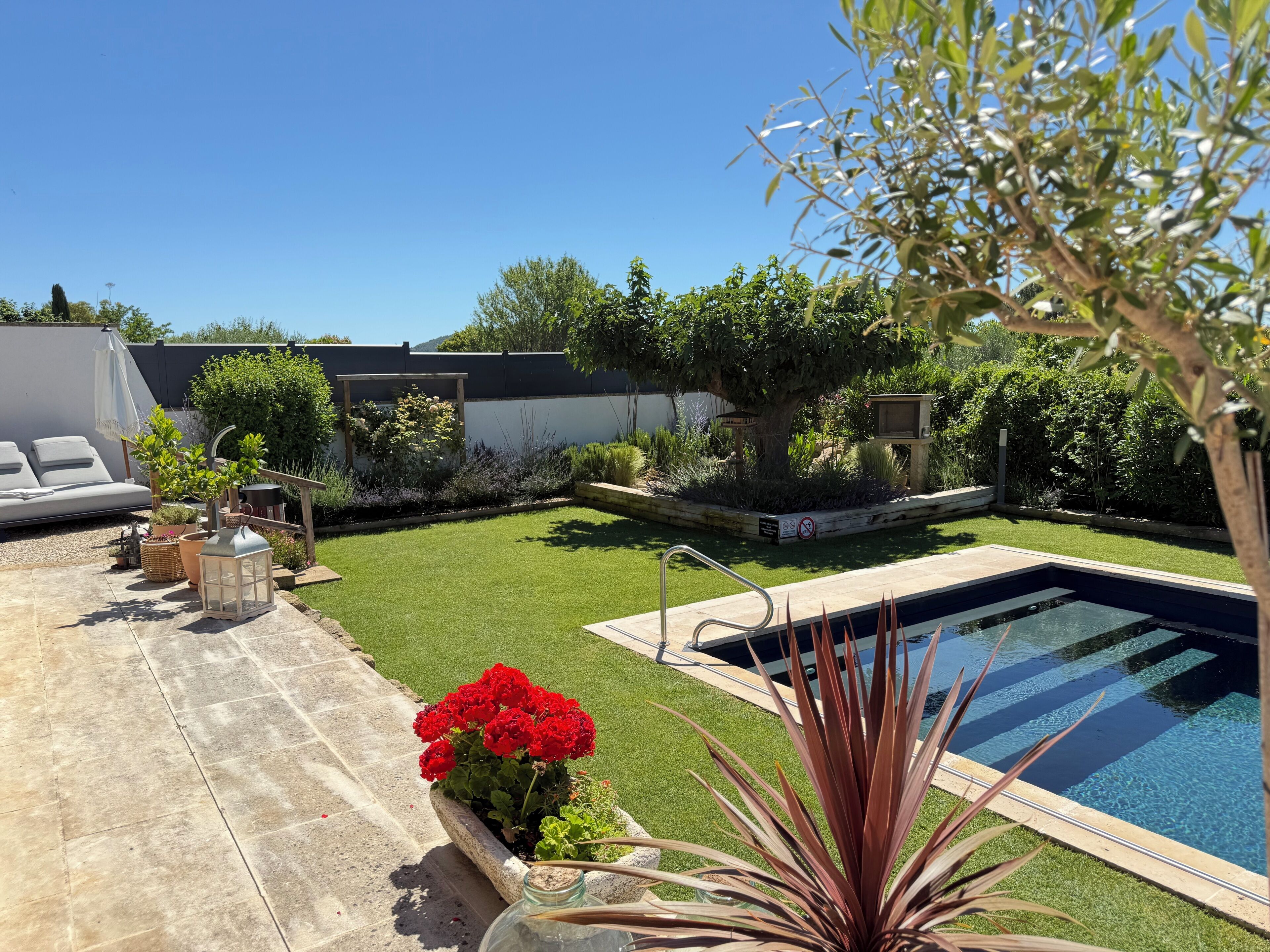 Un patio trasero con piscina, césped y un área de estar con una silla blanca y una mesa.