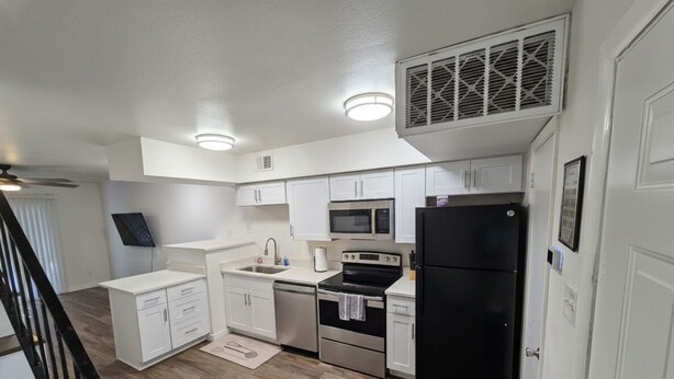 A modern kitchen with white cabinets, a black refrigerator, a microwave, an oven, and a dishwasher.