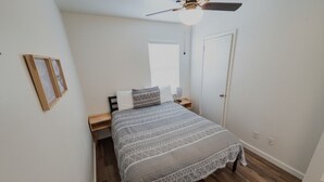 A bedroom with a bed, a ceiling fan, a door, and a window.