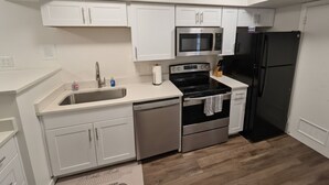 A compact kitchen with white cabinets, a stainless steel microwave, a black refrigerator, and a dishwasher.