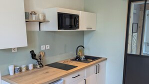 Een kleine keuken met witte kastjes, een houten aanrecht, een zwarte magnetron en een kleine koelkast.
