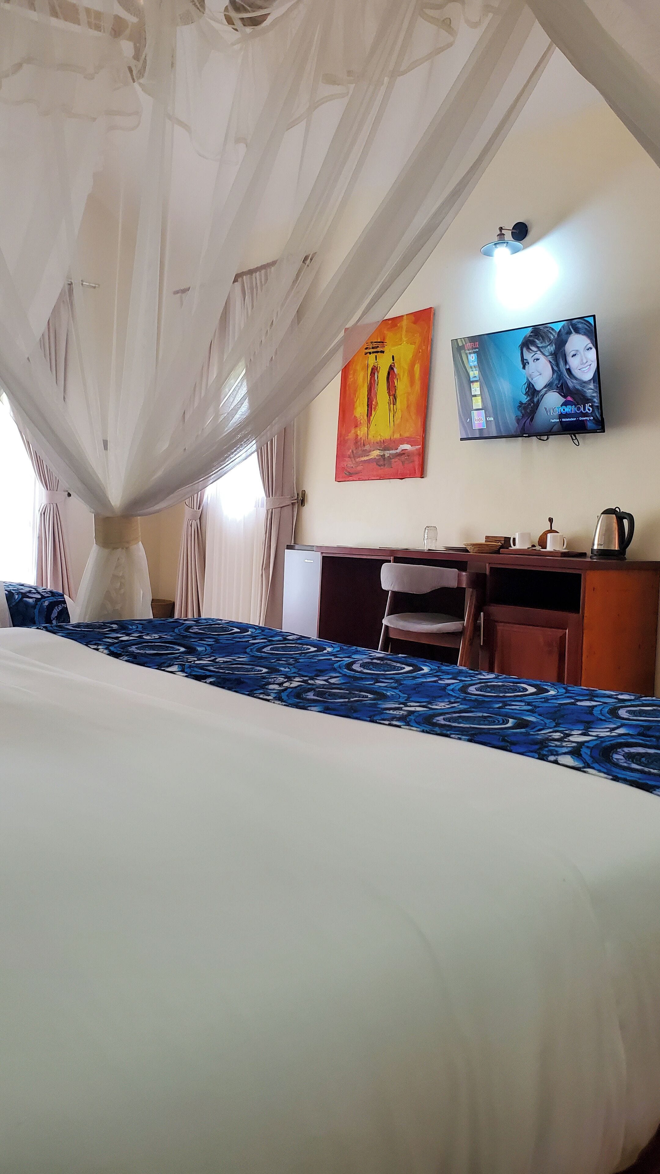 A hotel room with a bed, a desk, a chair, a television, and a mosquito net over the bed.