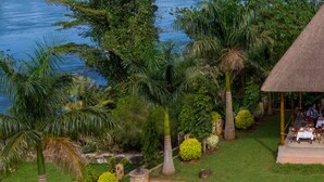A riverside view with lush greenery, a thatched-roof structure, and a stone pathway.