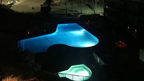 A swimming pool with a unique shape, surrounded by palm trees and a view of the ocean at sunset.