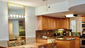 A kitchen with wooden cabinets, a granite countertop, a central island, and a dining area with chairs and a table.