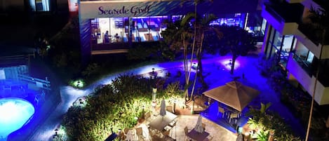 A Seaside Grill restaurant with outdoor seating, a swimming pool, and palm trees.