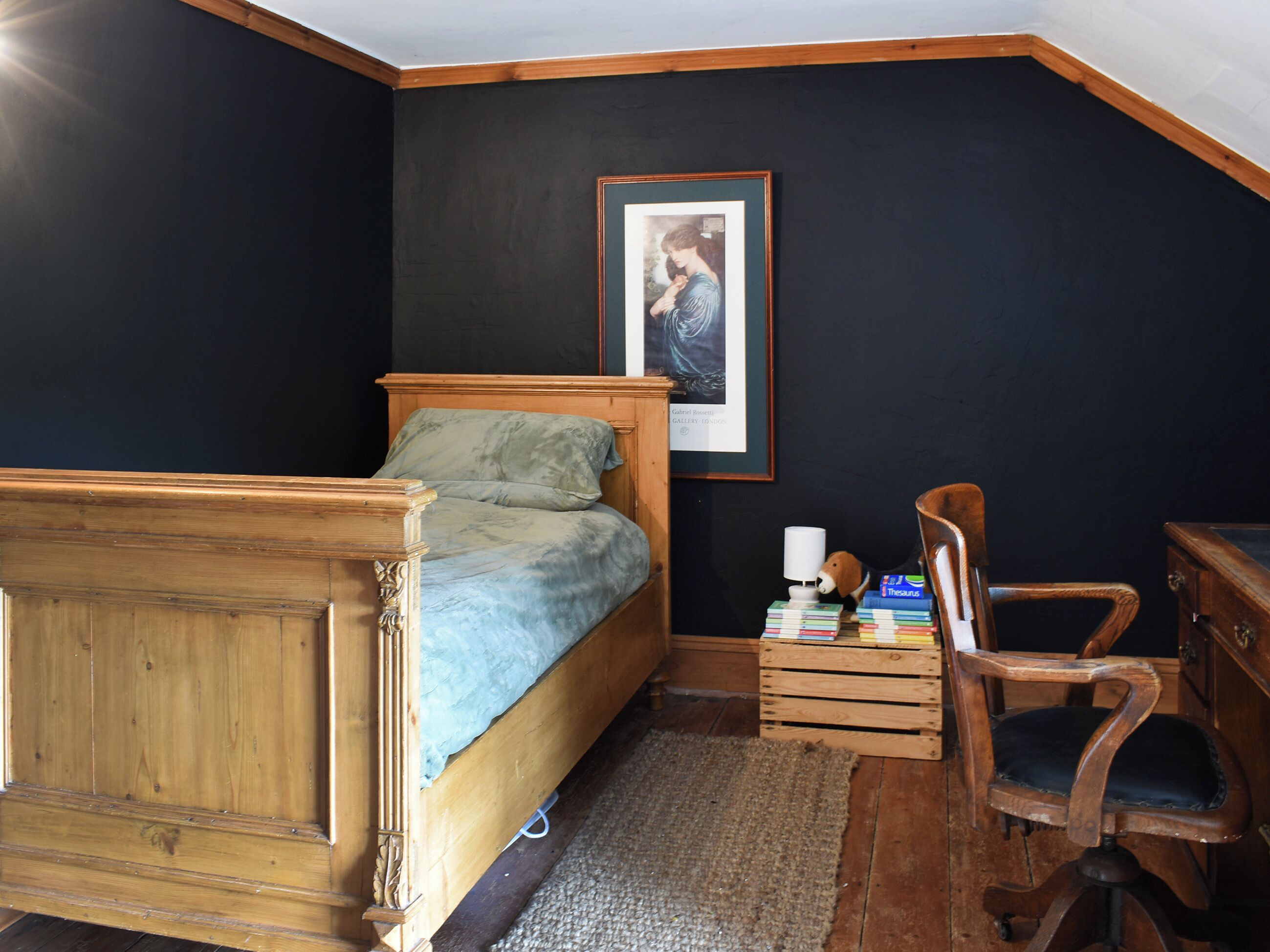 Une chambre à coucher avec un lit en bois, un bureau avec des livres, une chaise et un tableau encadré au mur.