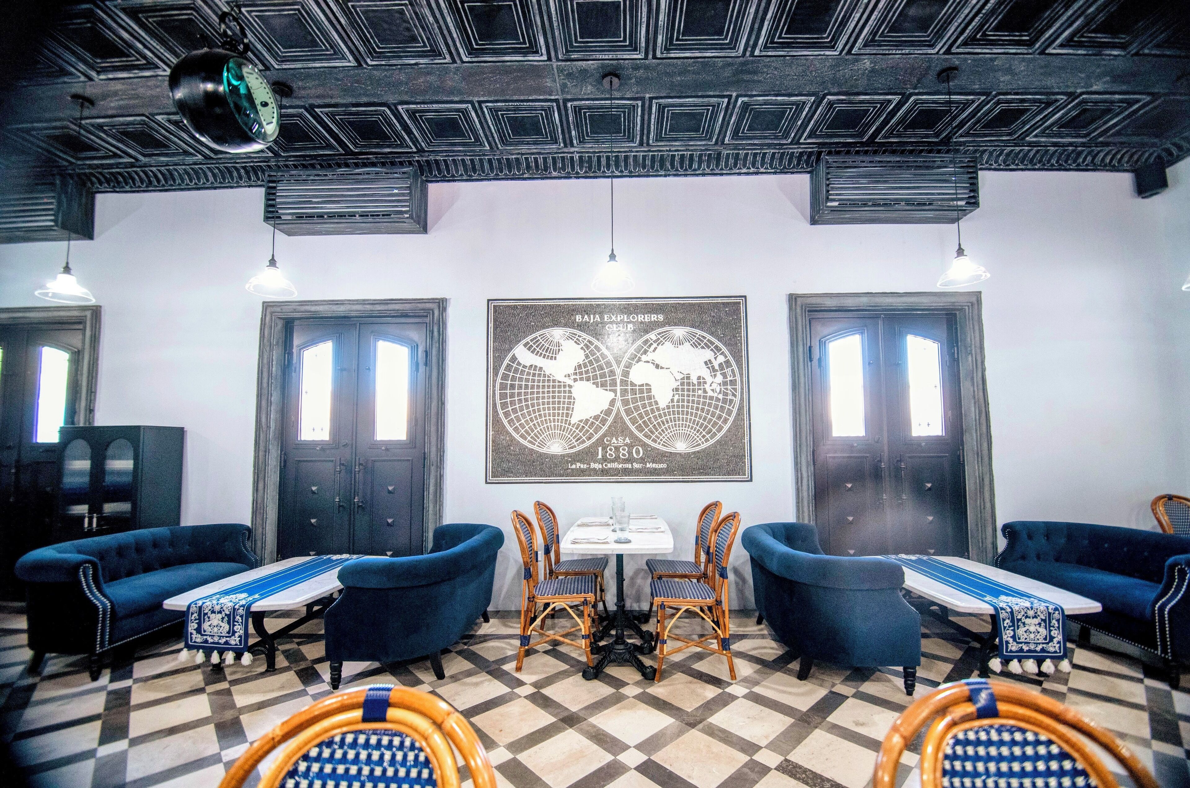 A room with checkered flooring, two blue sofas, a table with chairs, and a world map poster on the wall.