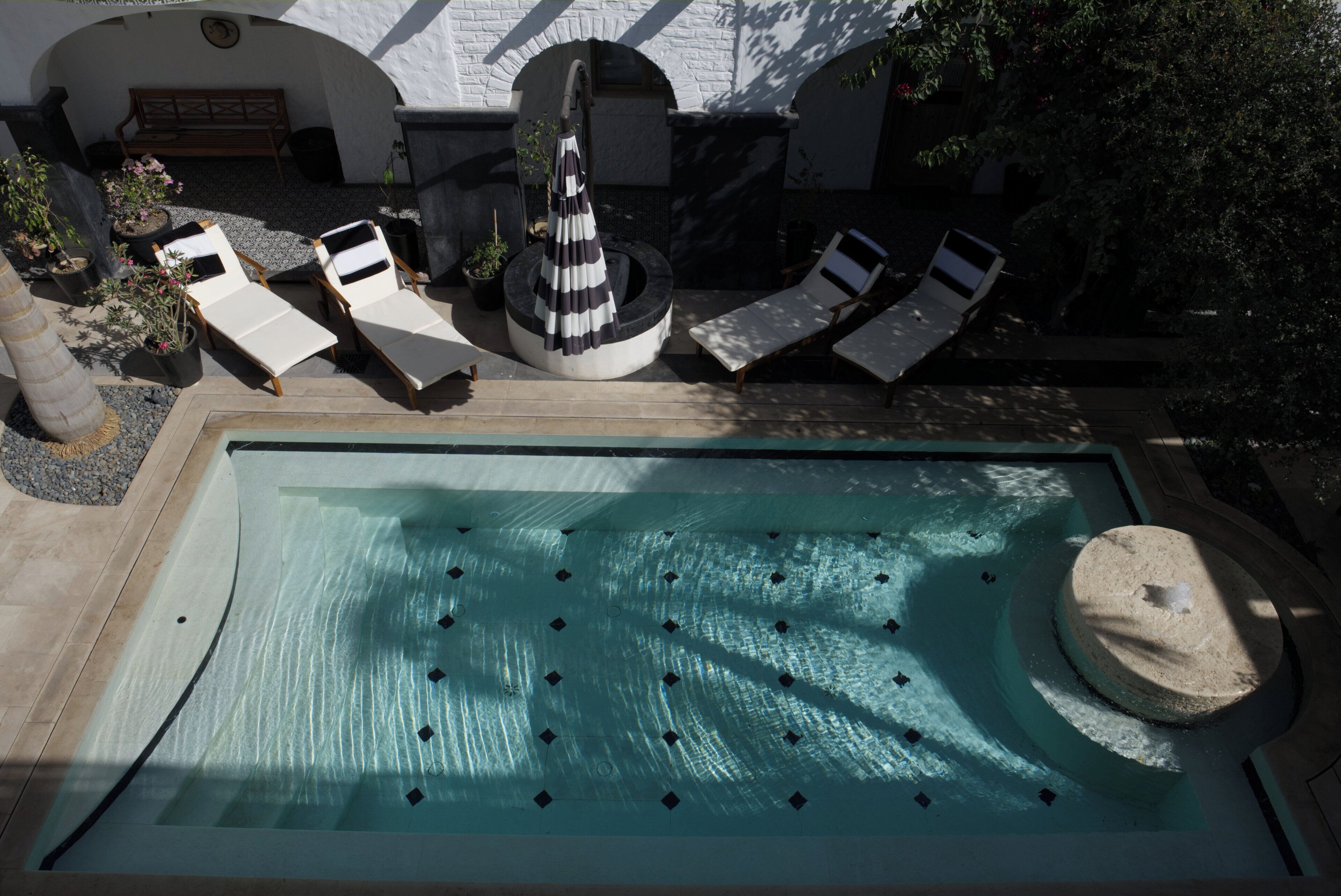 Un área de piscina con sillones de descanso, una bañera de hidromasaje circular y una fuente de piedra.