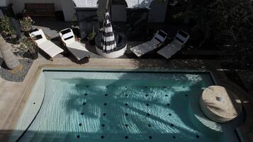 Un área de piscina con sillones de descanso, una bañera de hidromasaje circular y una fuente de piedra.
