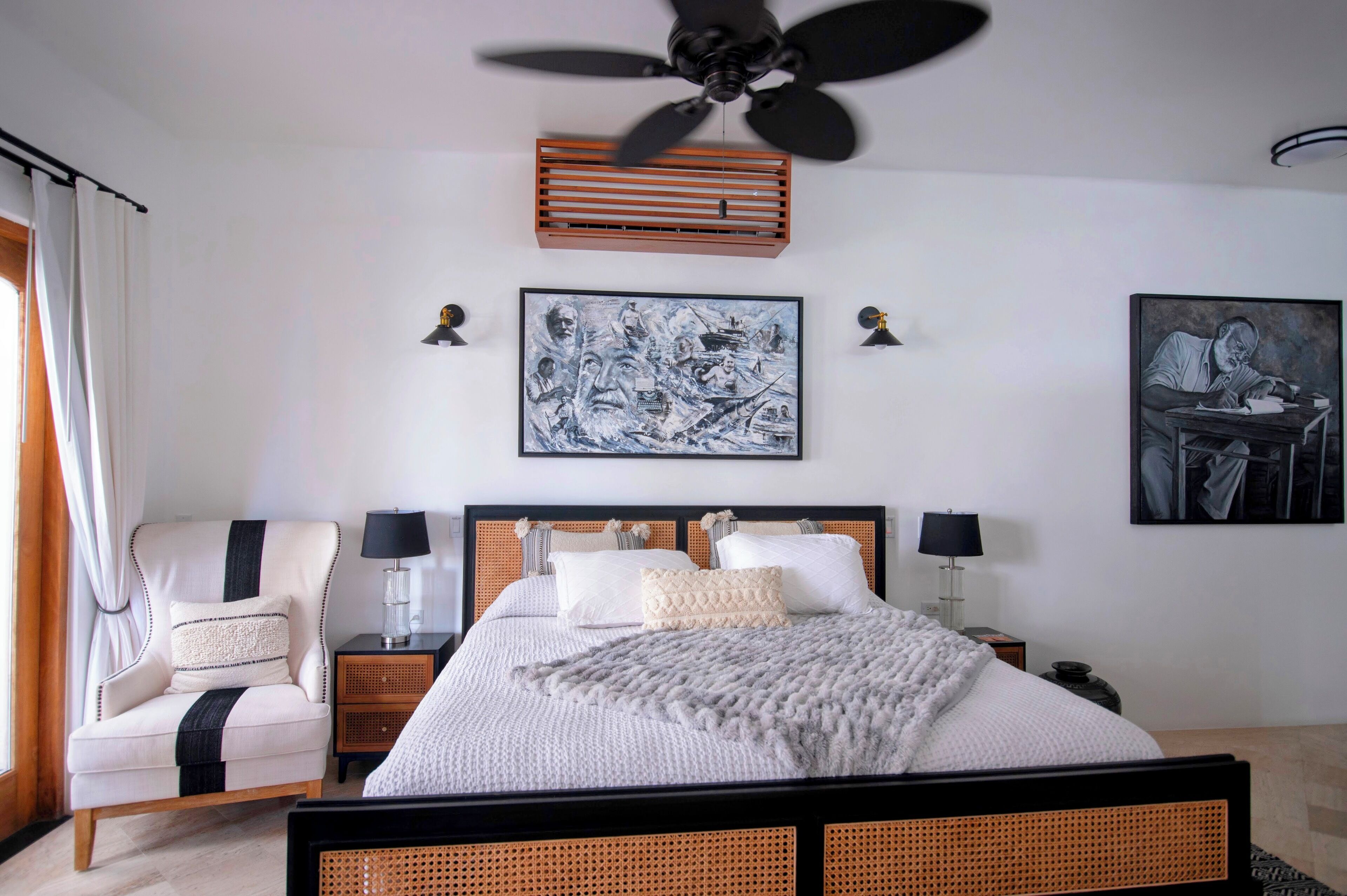 Ein Schlafzimmer mit Bett, Sessel, Nachttisch, Lampe und Deckenventilator.