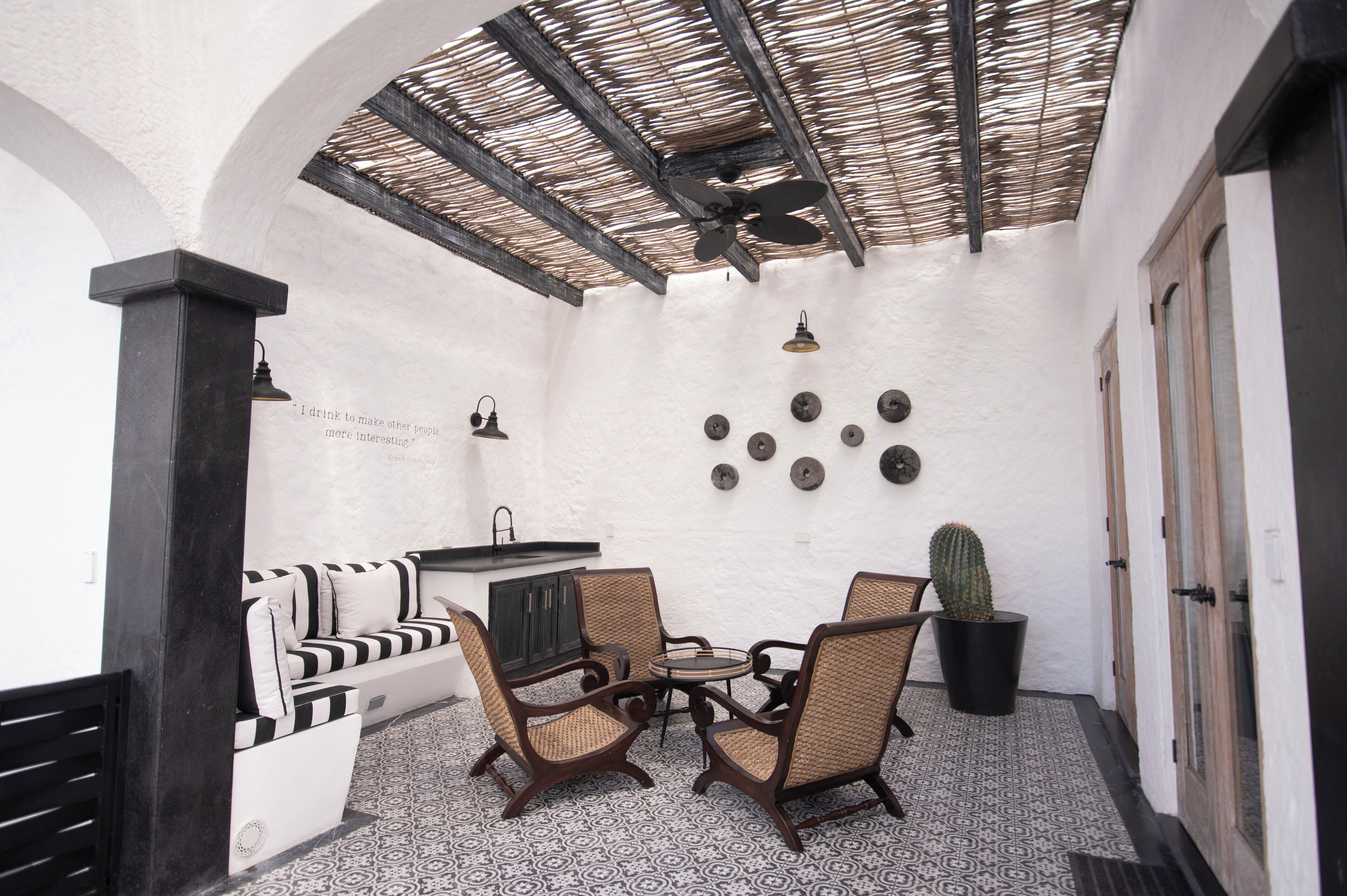 A cozy patio area with a black and white striped sofa, wicker chairs, a small round table, a cactus plant, and a ceiling fan.