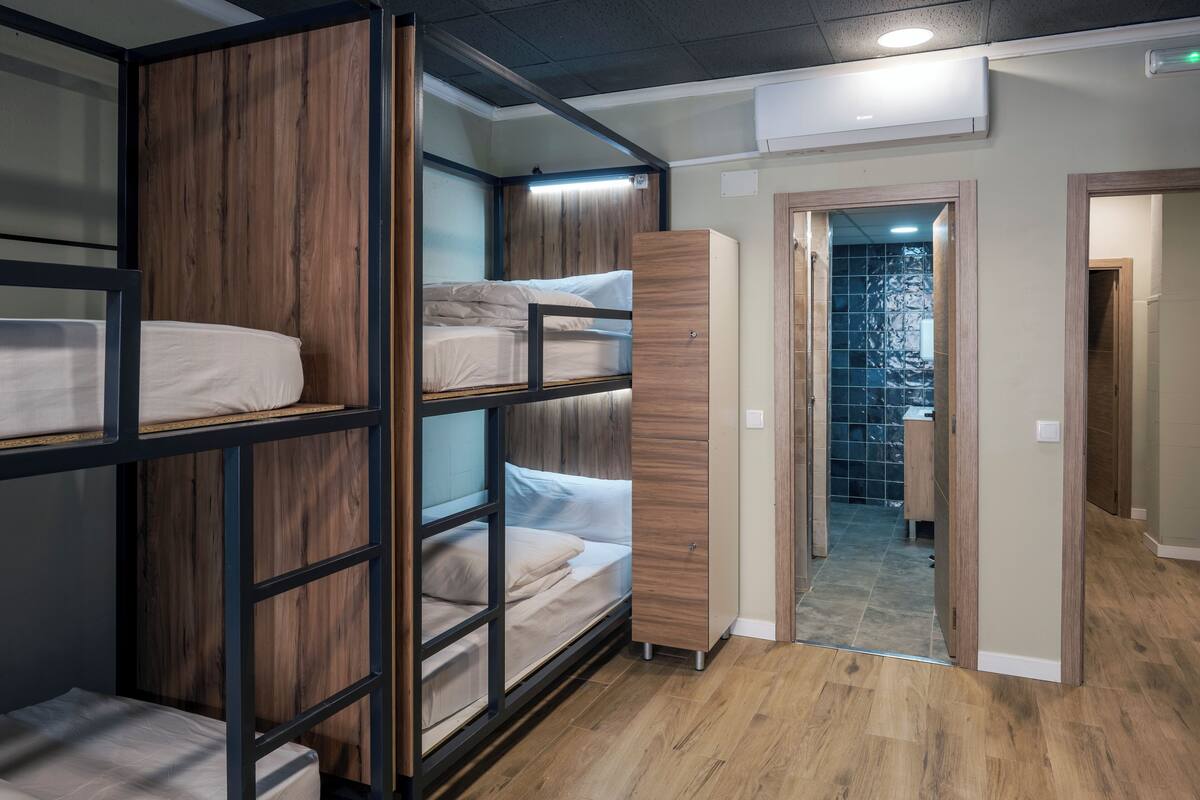 A bunk bed room with a wooden wardrobe and a bathroom visible through a glass door.