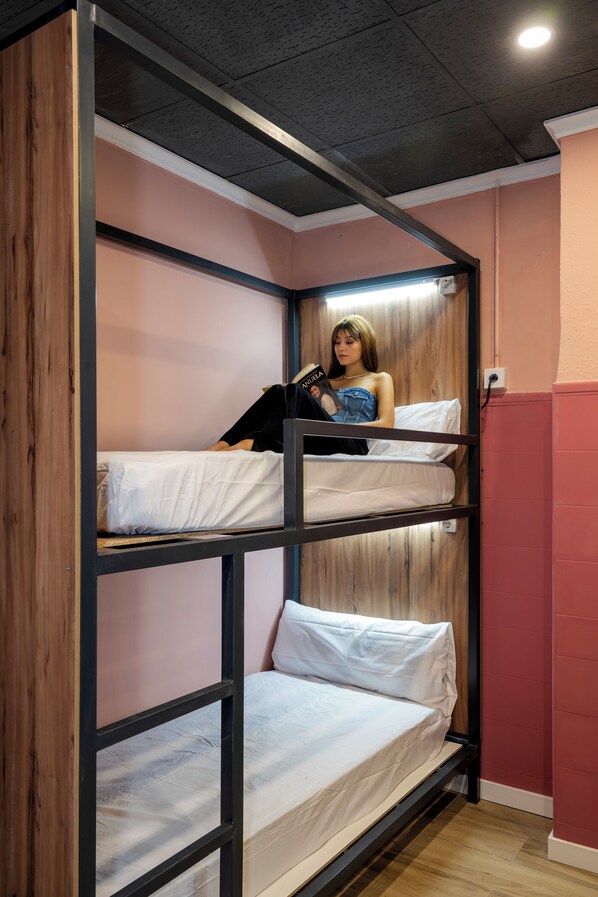 Une chambre avec un lit superposé doté d’une tête de lit en bois, une personne lisant un livre et un mur rose.