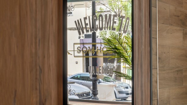 A mirror reflecting a welcome sign, a patterned floor, and a glimpse of the outside. - SOM HOSTEL BOUTIQUE  (Valencia)