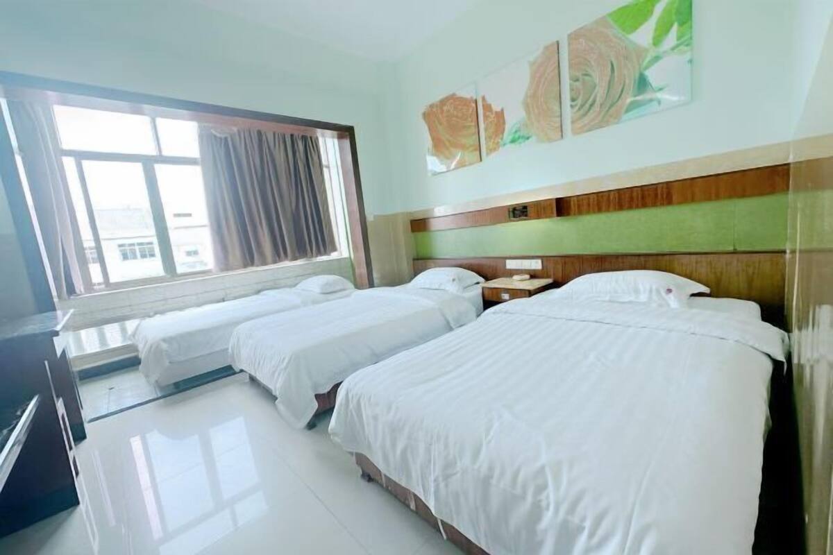 Habitación de hotel con dos camas, una ventana con cortinas, un televisor de pantalla plana y un cuadro floral en la pared.
