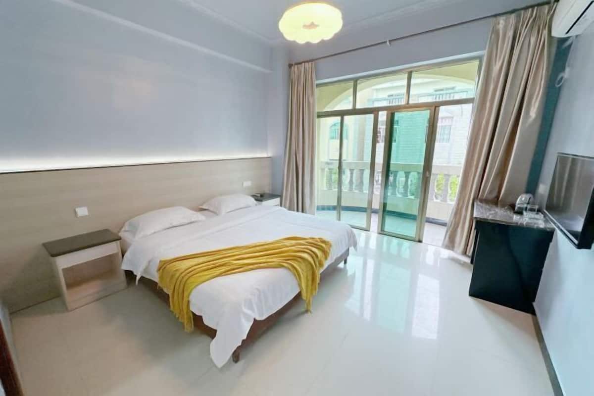 Una habitación de hotel moderna con una cama grande, una mesita de noche, un televisor y un balcón con cortinas.