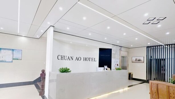 A hotel reception area with a modern design, featuring a reception desk labeled "CHUAN AO HOTEL" and a wooden bench to the right. - Qionghai Bojingchuanxi Hotel (Qionghai)