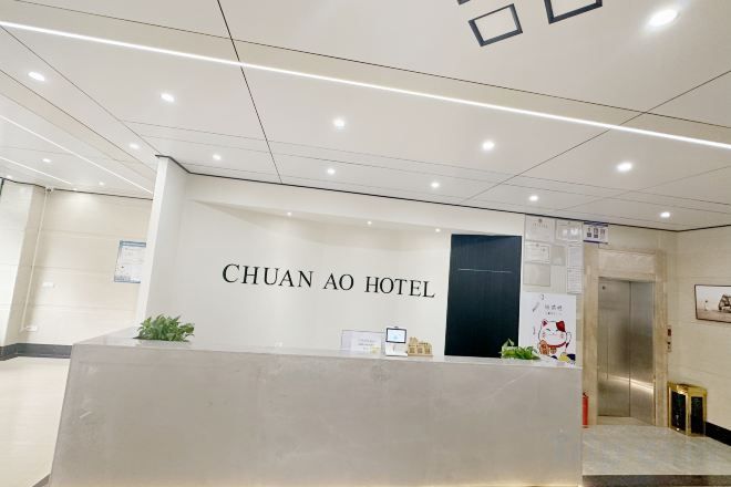 Zona de recepción de un hotel, con mostrador, pantalla digital y puerta al ascensor.