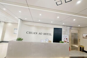 Un espace d’accueil d’hôtel comprenant un comptoir de réception, un écran numérique et une porte donnant accès à l’ascenseur.