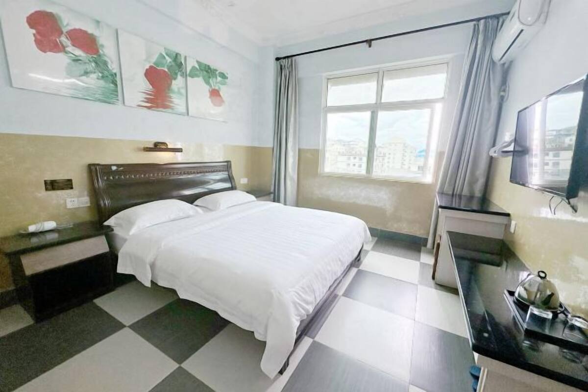 Una habitación de hotel con cama, escritorio, silla, televisión y ventana con cortinas.