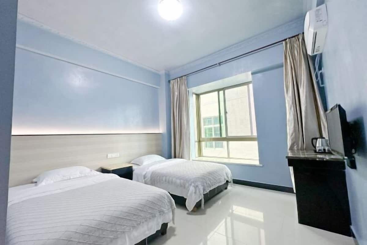 Una habitación de hotel con dos camas, una ventana con cortinas, un televisor de pantalla plana y un aire acondicionado instalado en la pared.