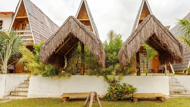 A row of thatched-roof cottages with a white wall in between, surrounded by greenery. - Chalé 3 Família (Angra dos Reis)