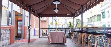 An outdoor patio with a covered seating area, tables, and a view of the street.