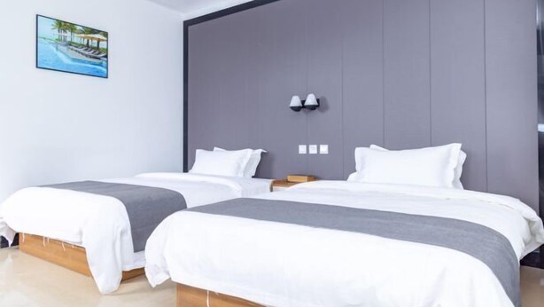 A modern hotel room with two beds, a large grey headboard, and a framed picture of a beach scene. - Caixia Inn (Shenzhen Xiyong Dapeng Branch) (Shenzhen)