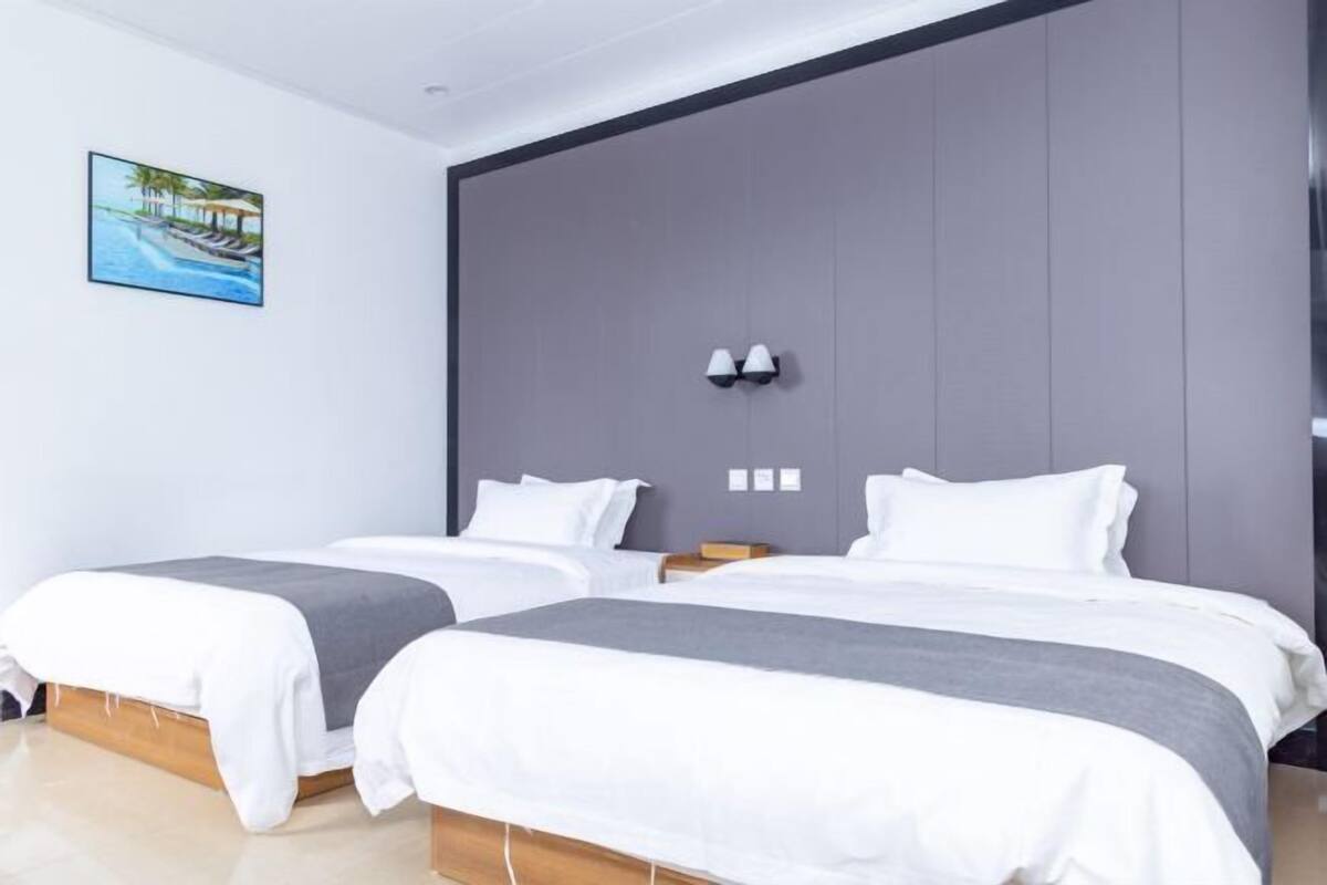 Una habitación de hotel moderna con dos camas, un cabecero gris grande y un cuadro enmarcado con una escena de playa.