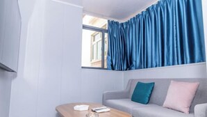 A room with a grey sofa, a wooden coffee table, and a window with blue curtains. - Caixia Inn (Shenzhen Xiyong Dapeng Branch) (Shenzhen)