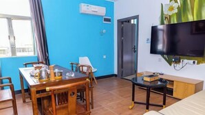 A room with a wooden dining table, chairs, a bed, a TV mounted on the wall, and a door. - Caixia Inn (Shenzhen Xiyong Dapeng Branch) (Shenzhen)