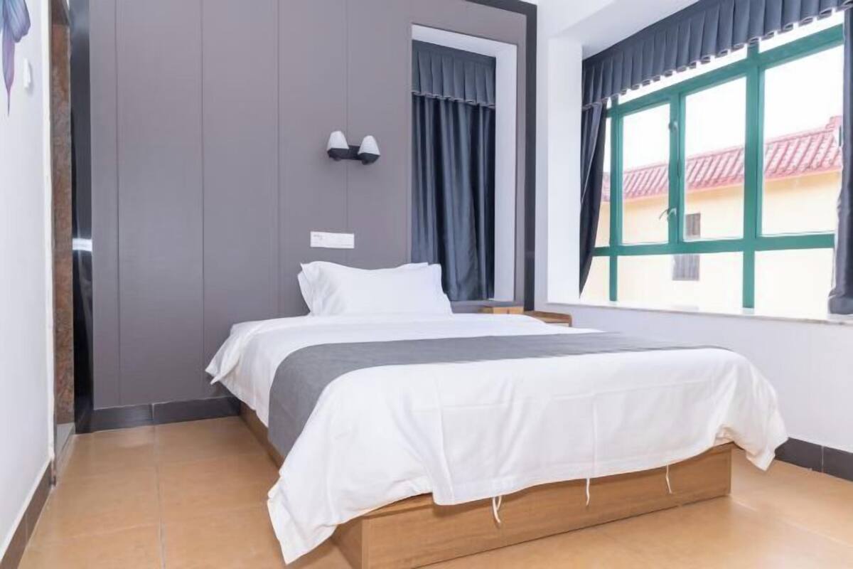 Un dormitorio con cama, ventana con cortinas y lámpara fijada a la pared.