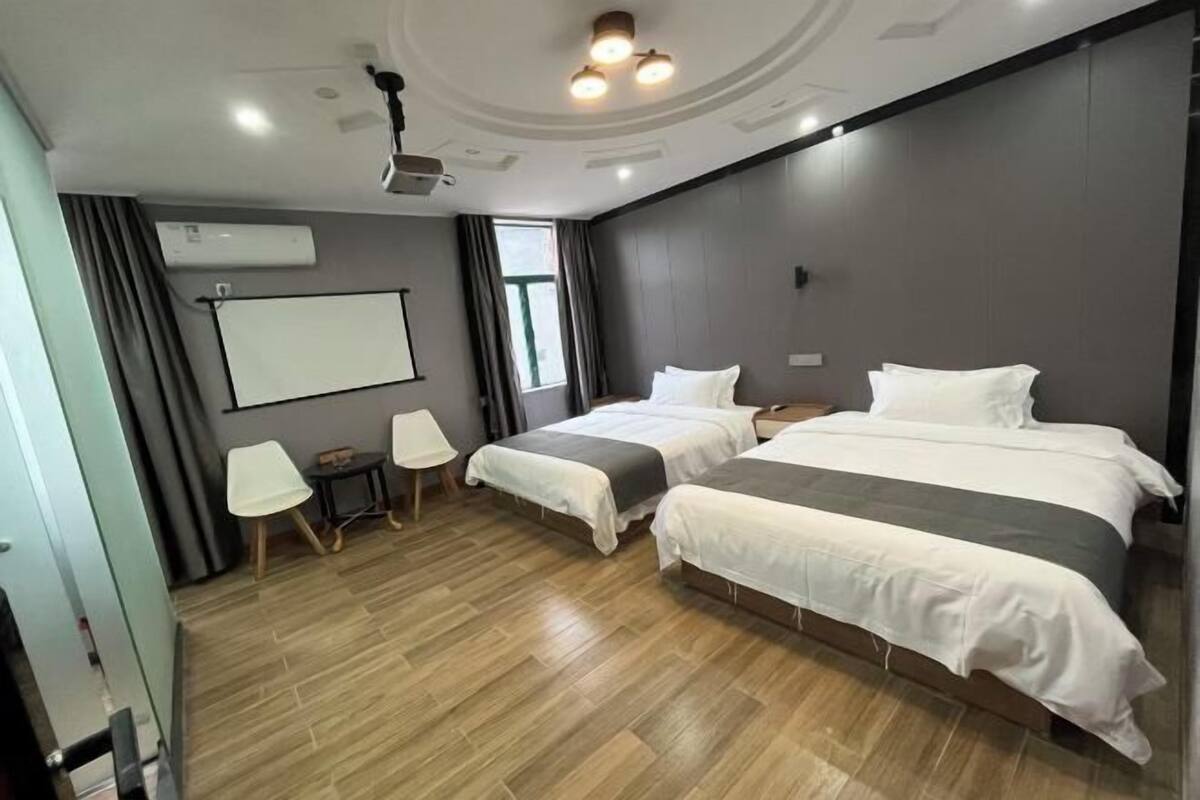 Habitación de hotel con dos camas, una pantalla de proyector, una mesita y una ventana.