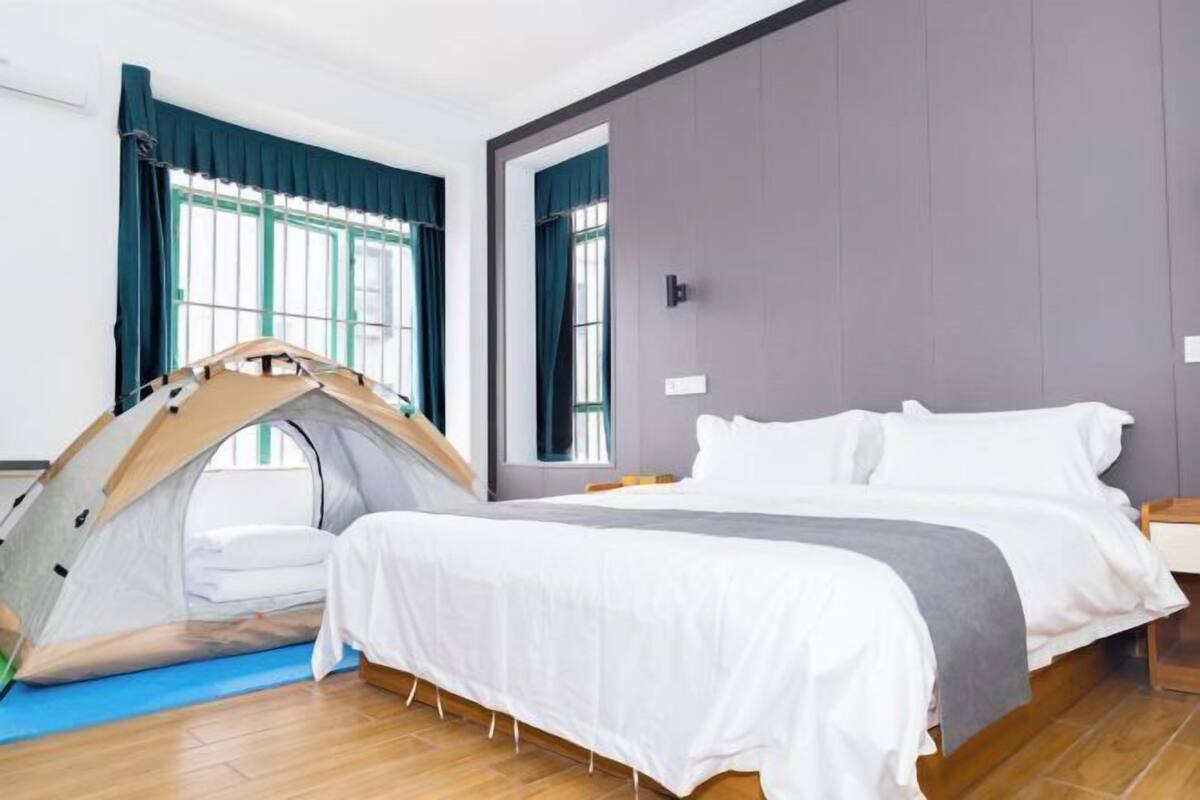 Un dormitorio con una estructura parecida a una tienda de campaña, una cama con ropa de cama blanca y una ventana con cortinas azules.