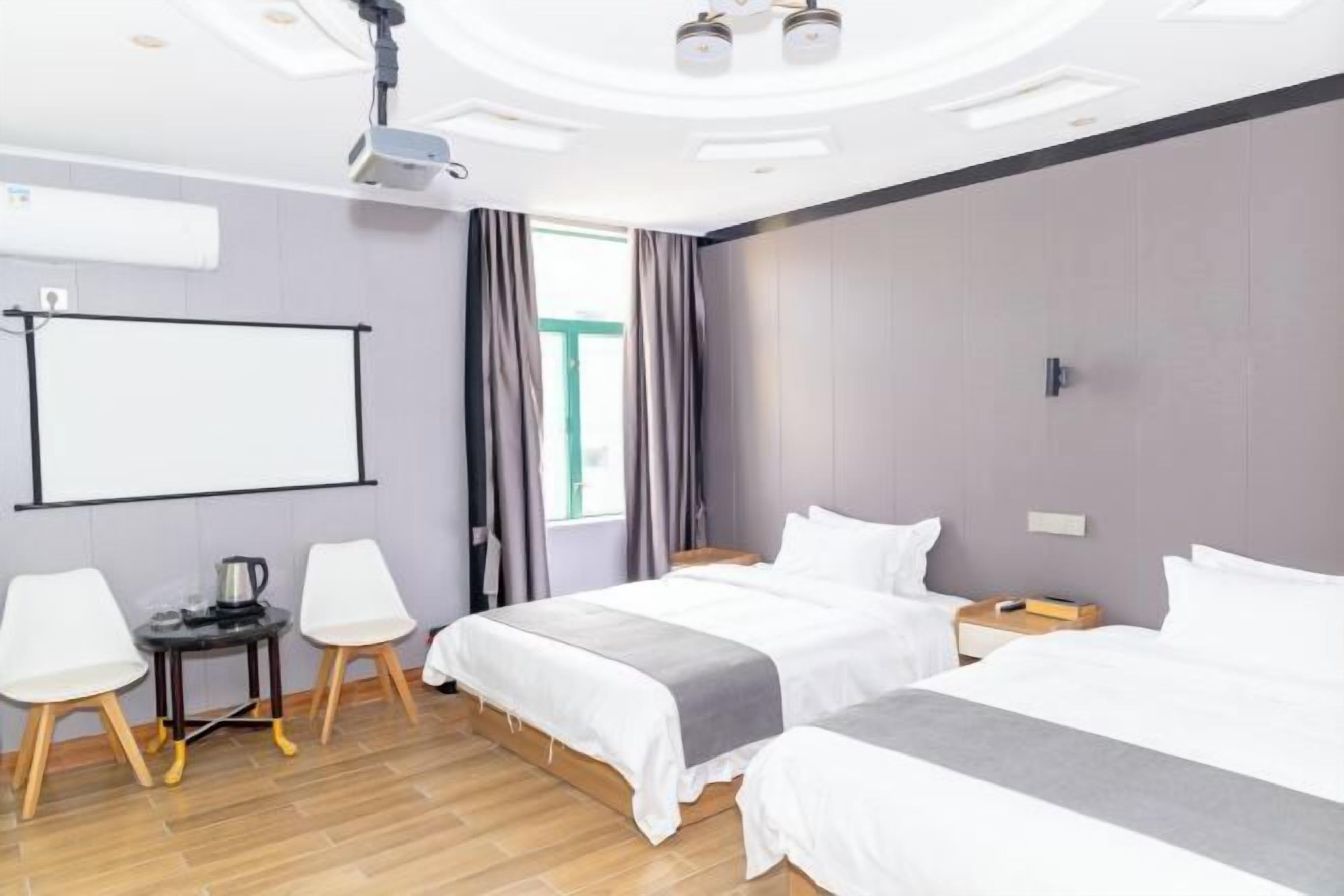 Habitación de hotel con dos camas, un proyector, una pizarra y una pequeña mesa con sillas.
