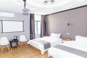 Una camera d'albergo con due letti, un proiettore, una lavagna e un piccolo tavolo con sedie.