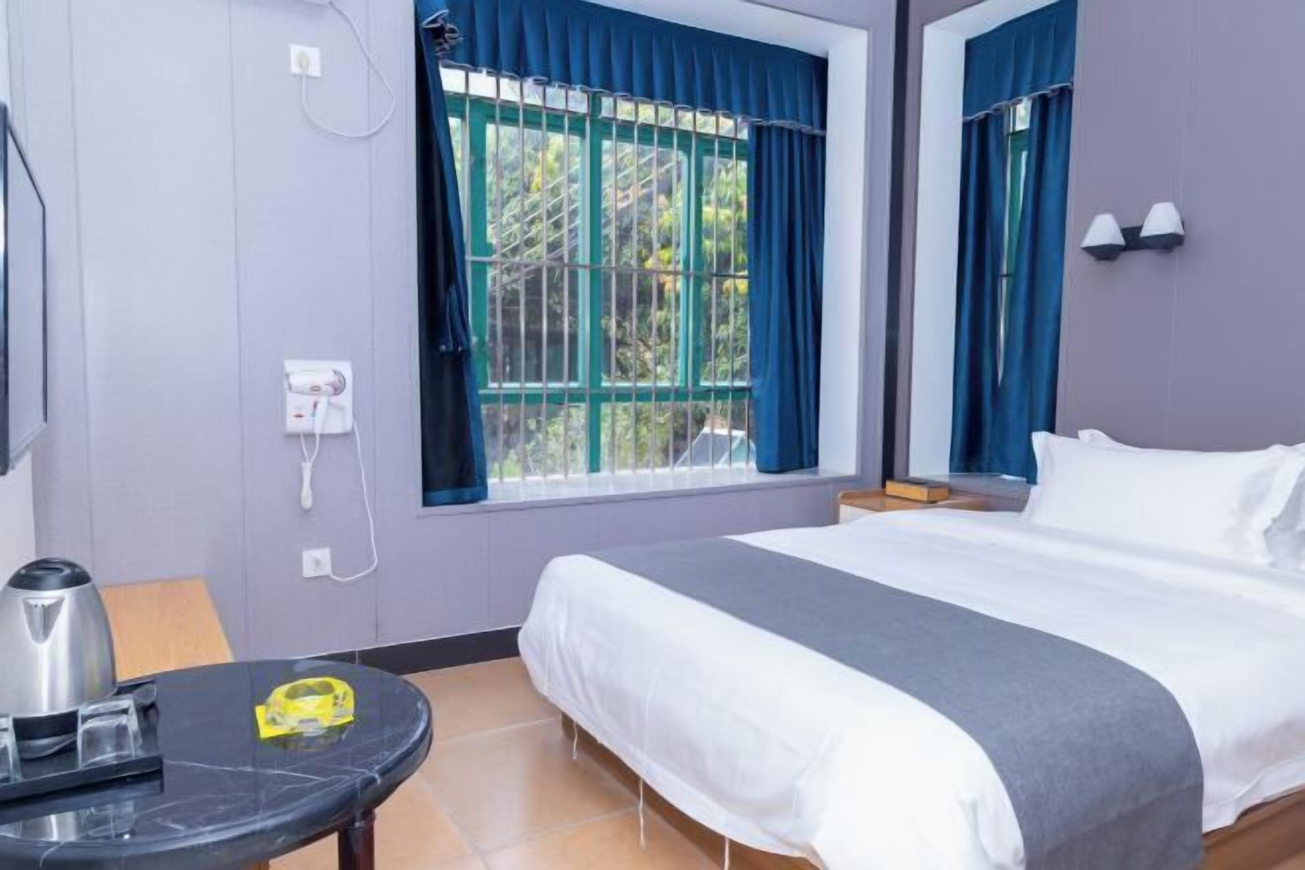 Una habitación de hotel con cama, una mesa con hervidor, toma de corriente y ventana con cortinas.