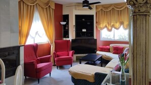 Ein Wohnzimmer mit Kamin, roten Sesseln, einer Couch, einem Fernseher und einem Deckenventilator.