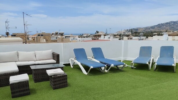 Eine Dachterrasse mit grüner Rasenfläche, weißem Sofa und blauen Lounge-Stühlen.