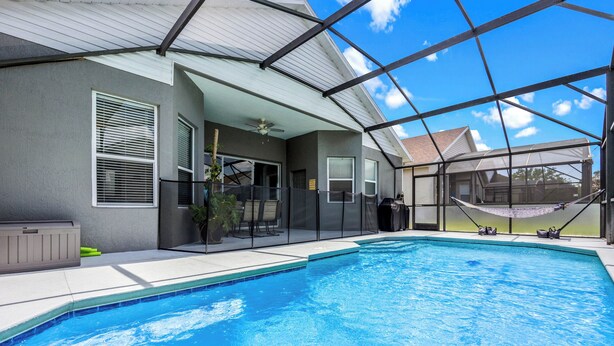 A swimming pool with a covered patio area, a ceiling fan, and a hammock.