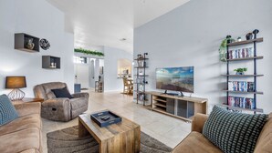 A modern living room with a sofa, coffee table, TV, bookshelf, and a dining area in the background.