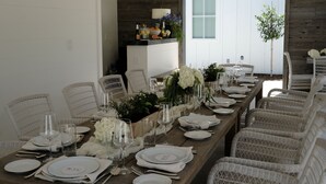 Une longue table à manger, dressée avec de l’argenterie blanche, des verres et un centre de table composé de fleurs blanches.