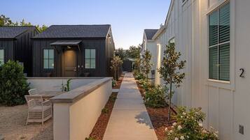 A residential street with houses, a concrete pathway, and small trees.