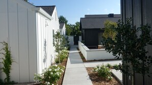 Un étroit sentier bordé de bâtiments aux couleurs claires et foncées, avec de petites plantes et un banc le long du chemin.
