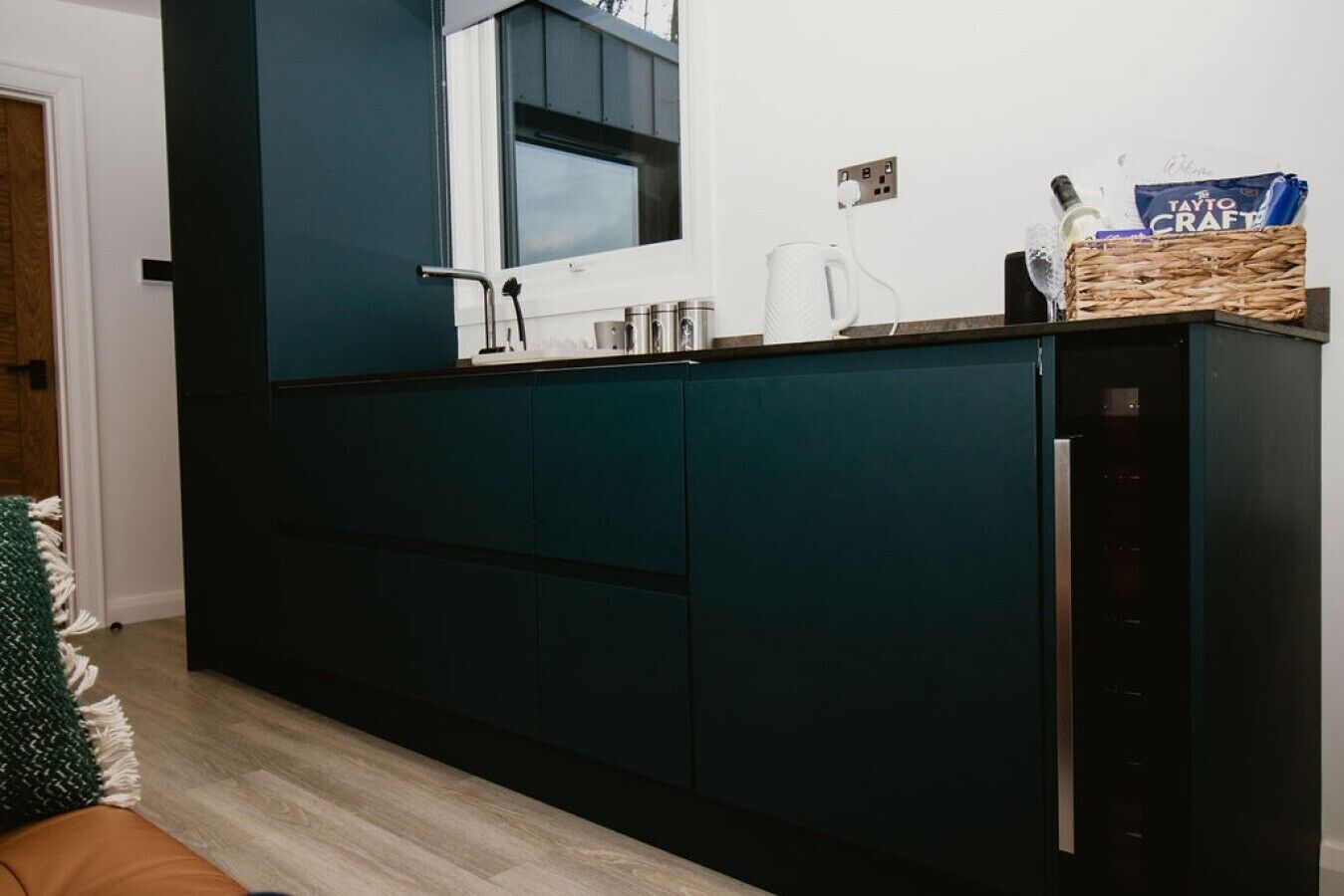 Une cuisine moderne avec des meubles de couleur bleu-vert foncé, un plan de travail blanc et une fenêtre au-dessus de l’évier.