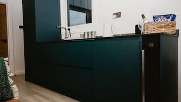 Une cuisine moderne avec des meubles de couleur bleu-vert foncé, un plan de travail blanc et une fenêtre au-dessus de l’évier.